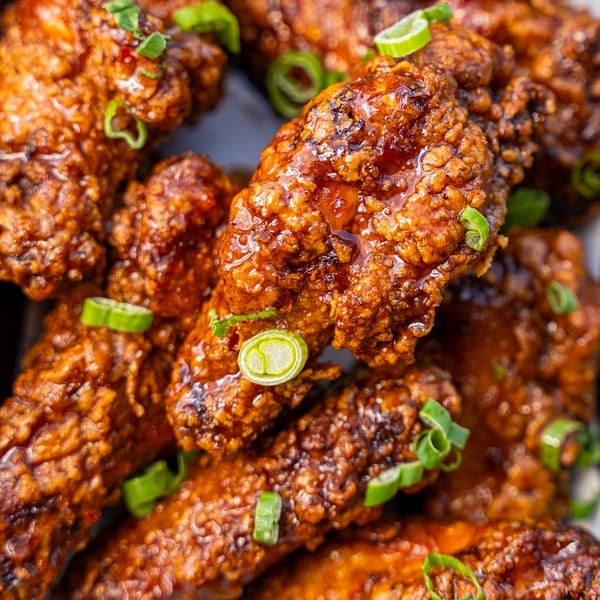 Close-up of crispy fried chicken wings coated in a glossy, sweet, and spicy sauce, garnished with green onions.