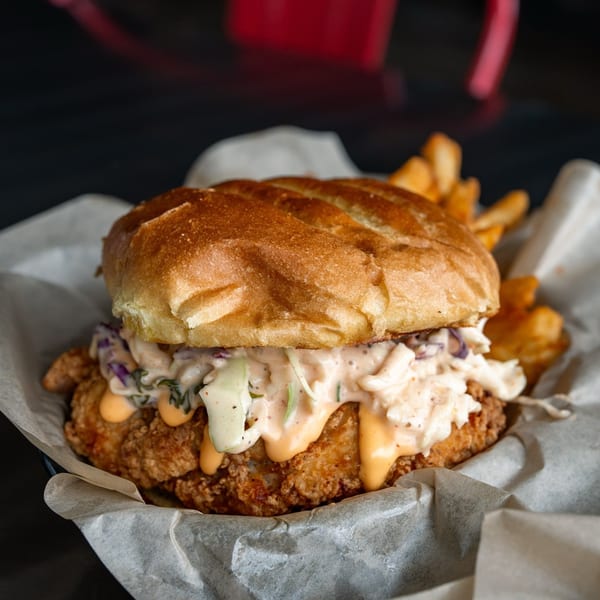 Crispy fried chicken sandwich with coleslaw and special sauce, served with fries in a basket.