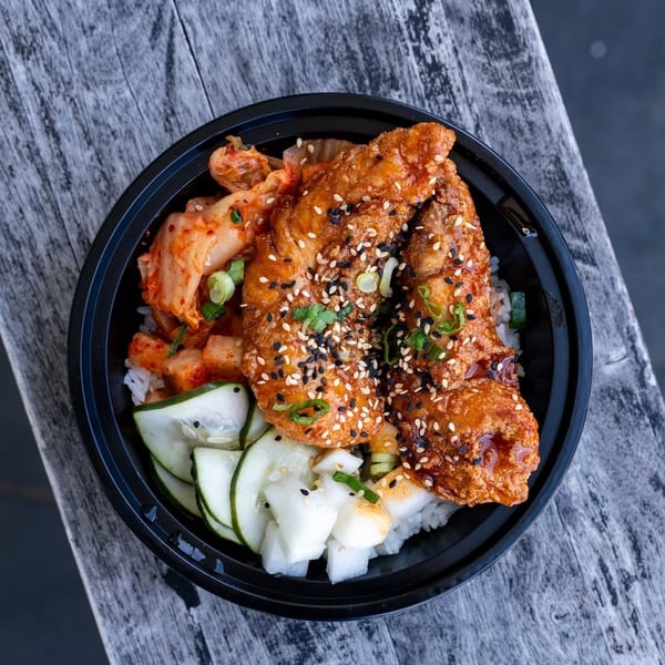 Crispy fried chicken with sesame seeds, kimchi, pickled cucumbers, and daikon over rice.